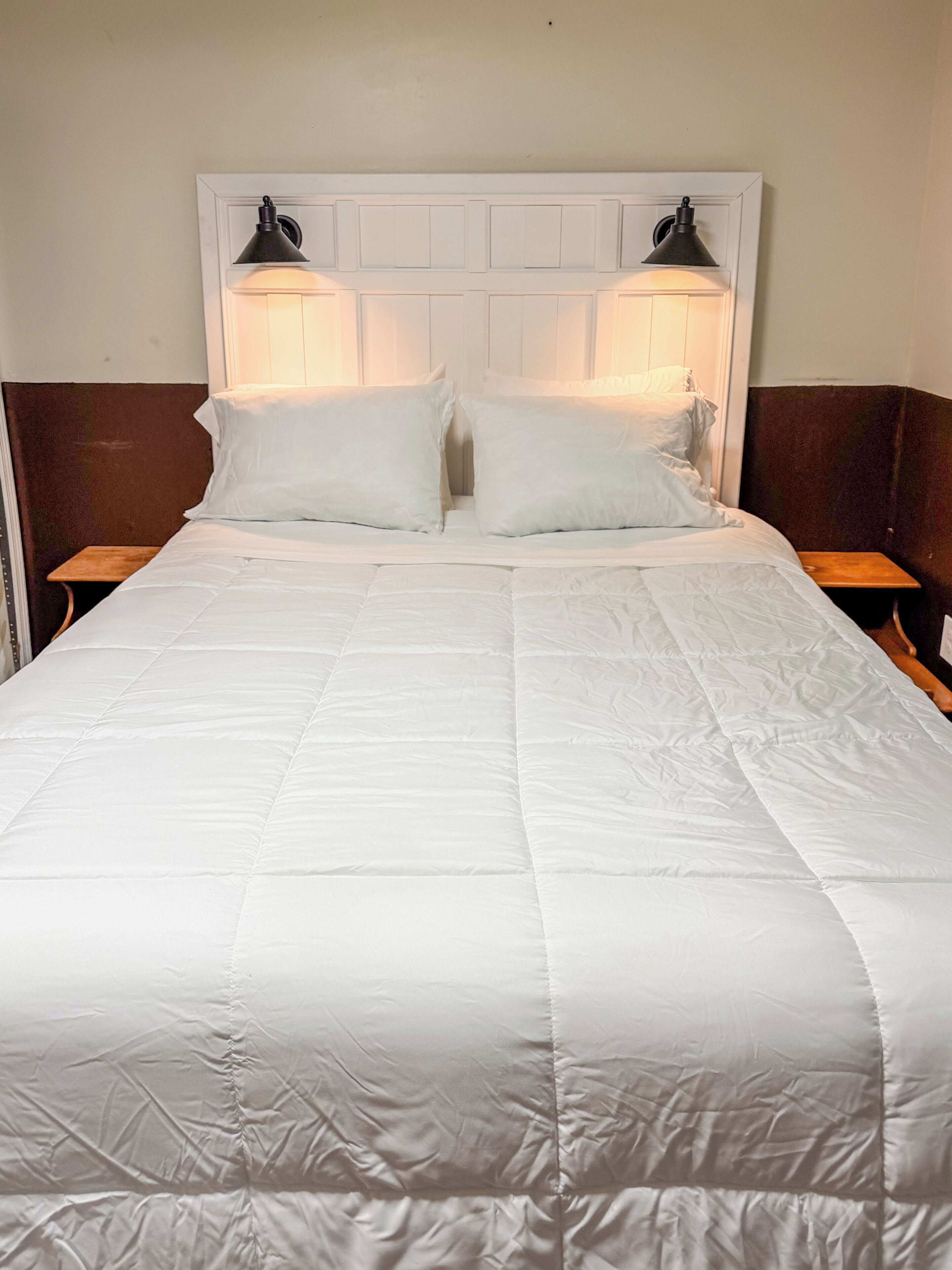 A neatly made bed with a white duvet, two bedside lamps, and a wooden nightstand.