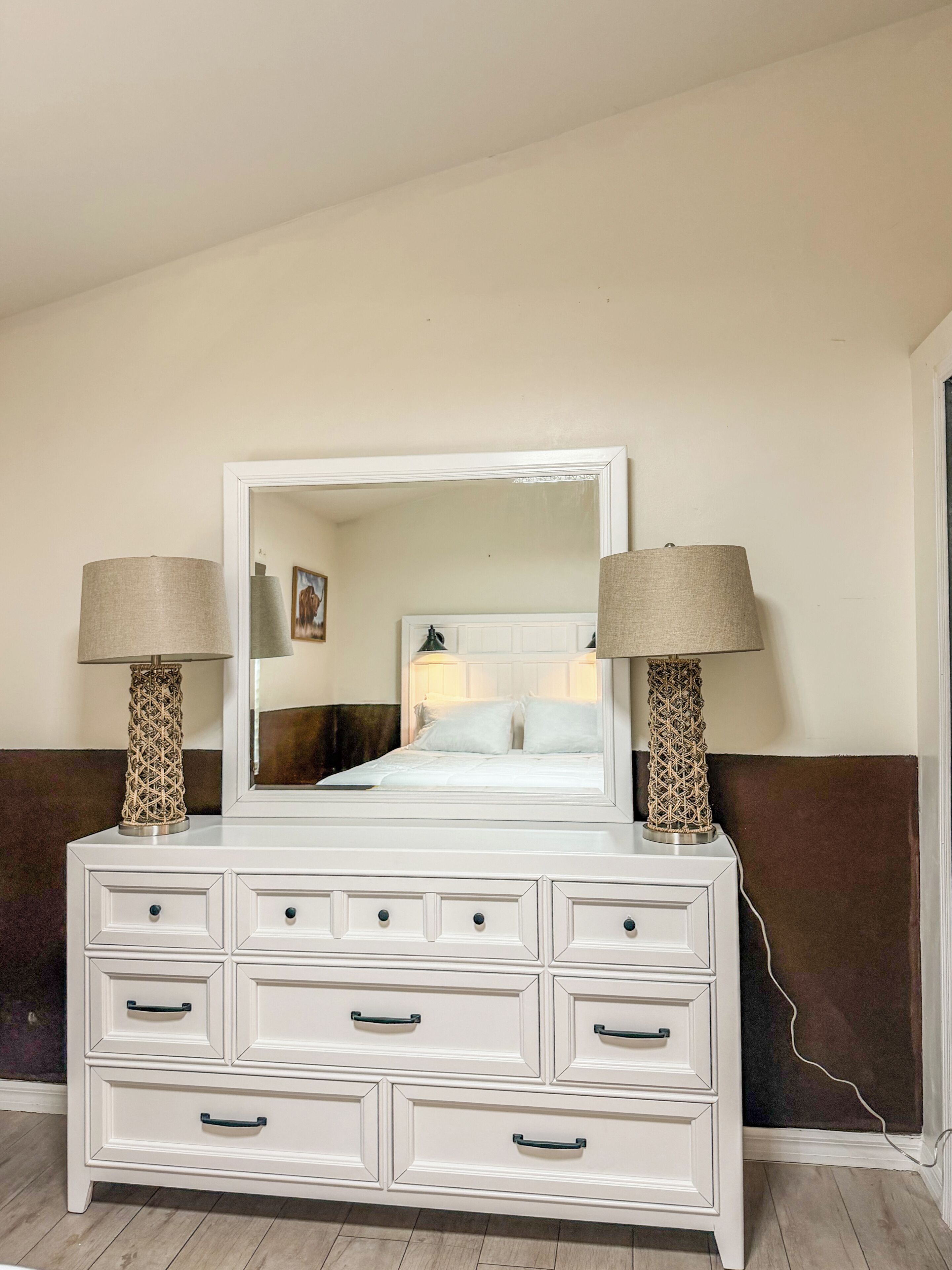 A white dresser with drawers and a mirror above it, flanked by two lamps with patterned bases.