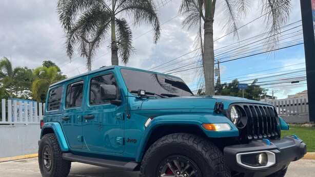 Ein türkisfarbener Jeep mit Geländereifen auf einer Betonfläche geparkt.