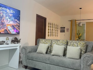 A living room with a grey sofa, decorative wall art, a flat-screen TV, and a small table with a decorative elephant. - Spacious Family Apartment With Pool Access in Santiago (Santiago de los Caballeros)