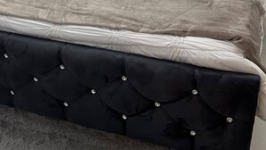 Ein Bett mit einer gesteppten Kopfstütze, einer grauen und weißen Bettdecke und mehreren Kissen.