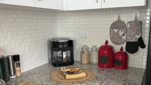 Eine Küche mit weiß gefliestem Fliesenspiegel, einer Kaffeemaschine, Gewürzgläsern und aufgehängten Topflappen.
