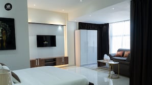 Een moderne hotelkamer met een bed, een televisie, een kledingkast, een bank en een klein tafeltje.