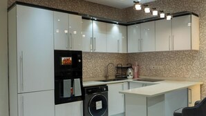 Een moderne keuken met witte kastjes, een inbouwoven, een wasmachine en een bar met een stoel.