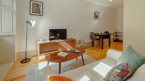 A modern living room with a flat-screen TV, wooden entertainment unit, a dining area with a table and chairs, and a sofa with a patterned cushion. - Apartment  by Interhome (Porto)