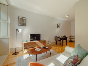 Ein modernes Wohnzimmer mit Flachbildfernseher, einer Holzunterhaltungsecke, einer Essecke mit Tisch und Stühlen sowie einem Sofa mit gemustertem Kissen.