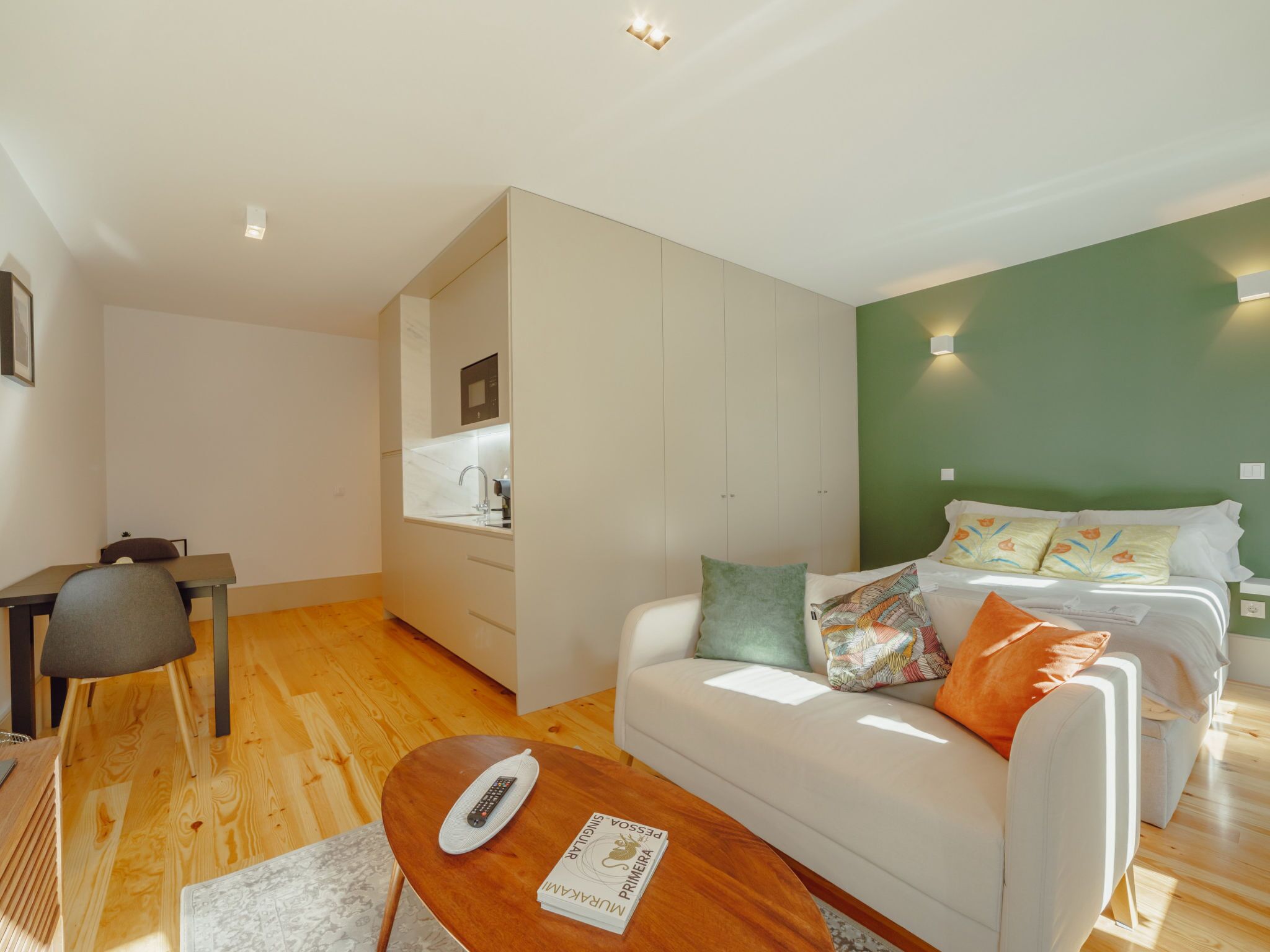 Een moderne slaapkamer met een witte bank, een houten salontafel en een groene accentmuur.