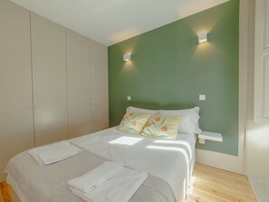 Ein Schlafzimmer mit einem Bett, weißen Bettwäsche, einer grünen Wand und einem Holzboden.