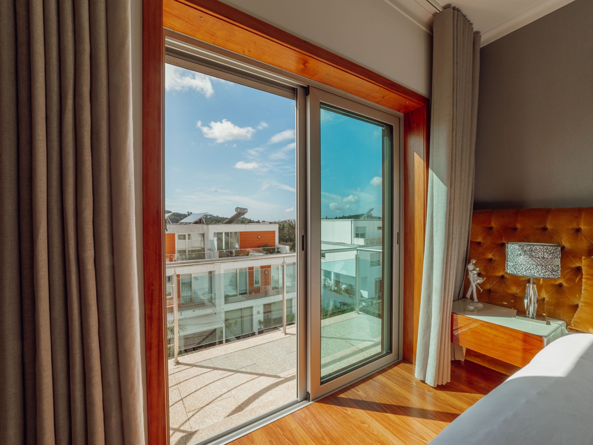 Ein Hotelzimmer mit einer großen Schiebeglasdoor zum Balkon, einem gepolsterten Kopfteil und einem Nachttisch mit Lampe.