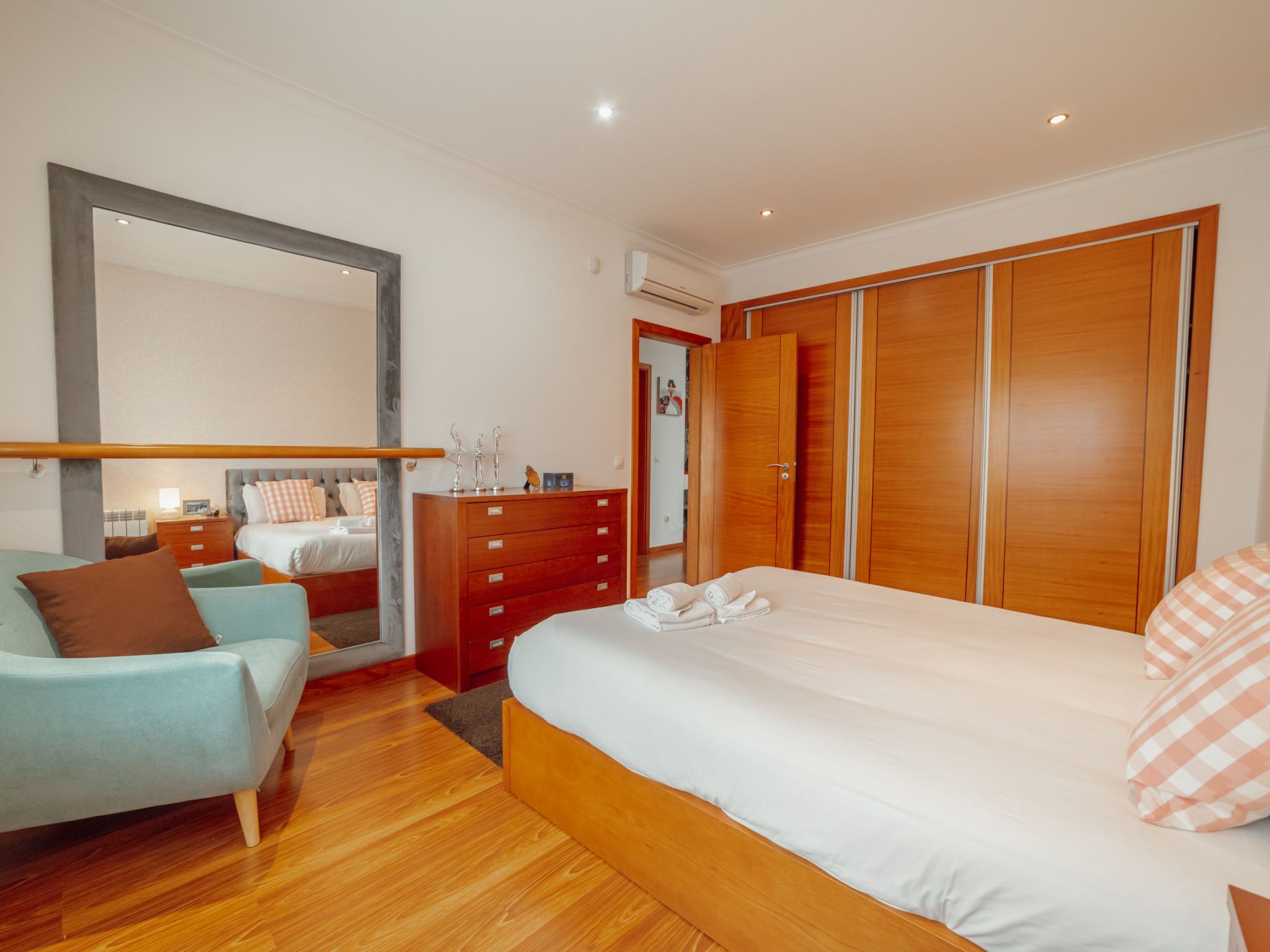 Een moderne slaapkamer met een groot bed, een dressoir, een kledingkast en een spiegel.