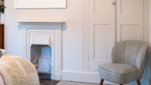 A room with a fireplace, a framed painting, a closed door, and a patterned chair. - Contemporary Coastal Chic: 3-Bed with Garden (Salcombe)