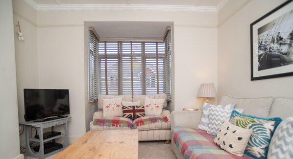 A living room with a television, a sofa, a coffee table, and a window with blinds.
