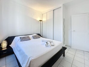Una habitació d'hotel amb llit, taulella de nit, làmpada i una porta.