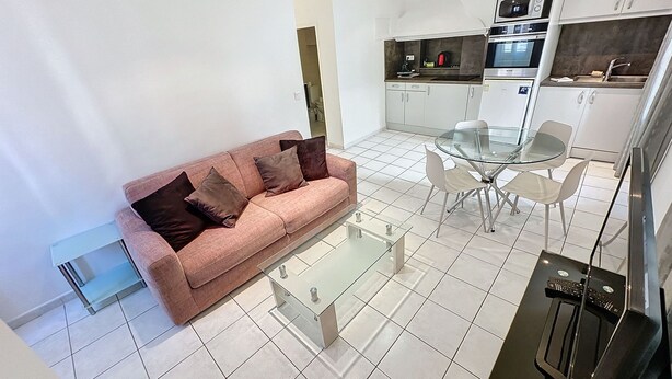 A modern living room with a sofa, a glass coffee table, and a dining area with a glass table and chairs. - Apartment  by Interhome (Cannes)