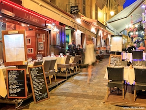 An outdoor dining area of a restaurant with tables set for guests, menus displayed, and a sign indicating the restaurant name. - Apartment  by Interhome (Cannes)