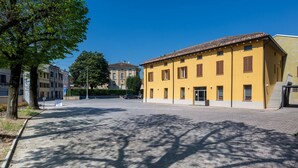 Una piazza lastricata con un edificio giallo, alberi e un cielo azzurro limpido.