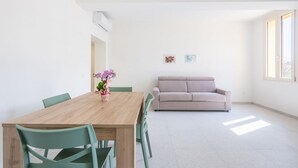 Un soggiorno moderno con un tavolo da pranzo in legno, sedie verdi, un divano beige e due quadri appesi al muro.
