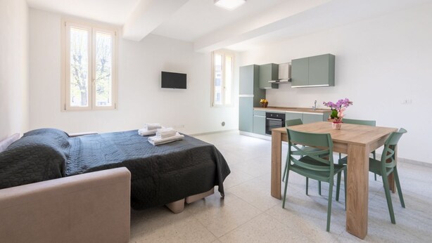 Una camera moderna con un letto, un tavolo da pranzo con sedie, un angolo cottura e una TV appesa al muro.