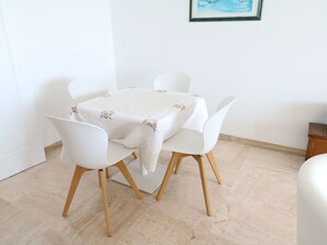 Ein Essbereich mit einem Tisch, vier Stühlen, einer weißen Tischdecke und einem gerahmten Bild an der Wand.