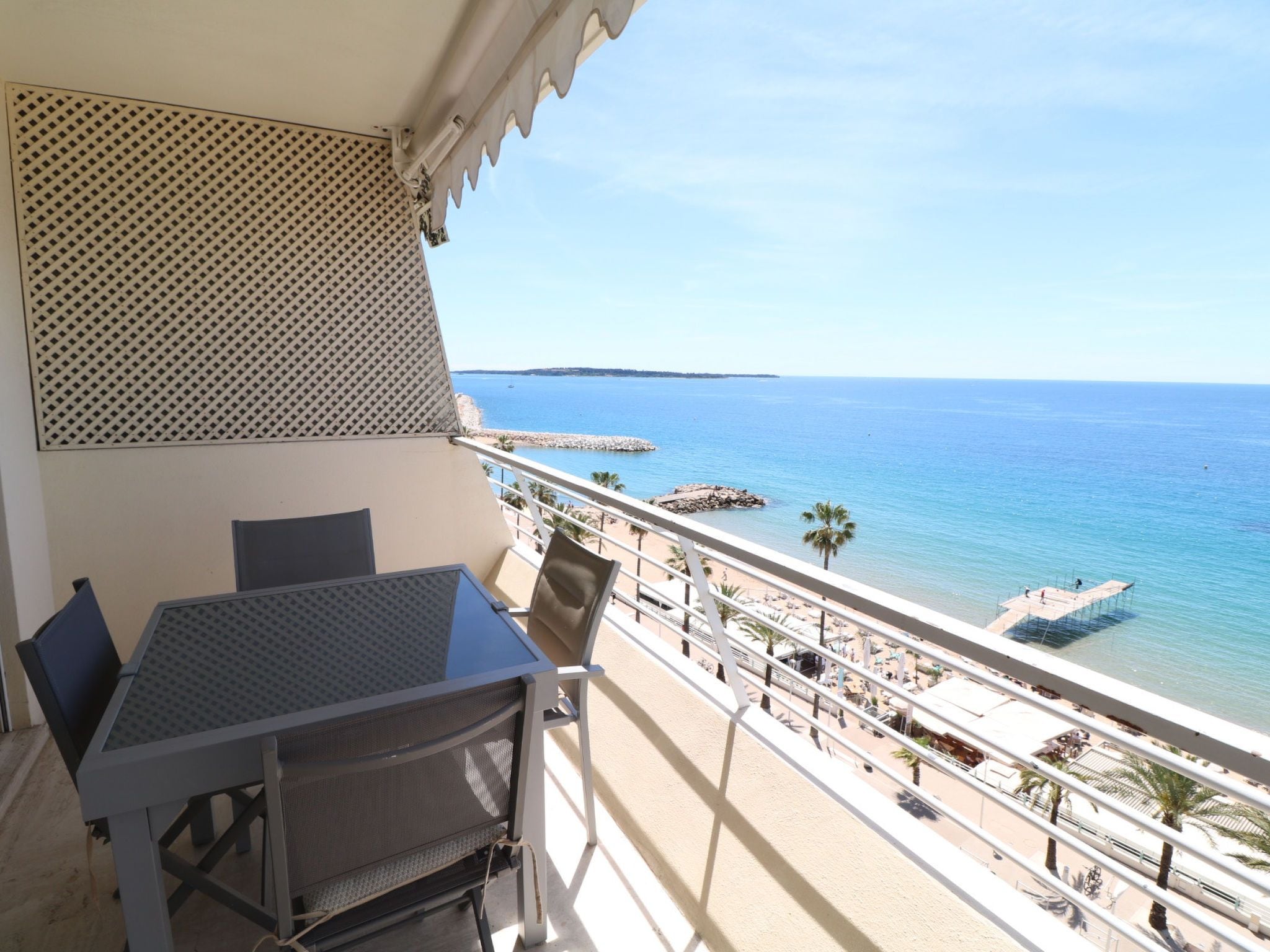 Ein Balkon mit Tisch und Stühlen, der Blick auf einen Strand mit freier Meer- und Landschaftsicht bietet.