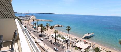 A balcony overlooking a beach with a road, palm trees, and a pier.
