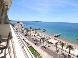 Ein Balkon mit Blick auf einen Strand, eine Straße, Palmen und einen Steg.