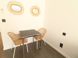 A small room with a table and two wicker chairs, a wall-mounted light fixture, and a power outlet. - Beautiful studio at the Grand Hotel 138 by Interhome (Cannes)