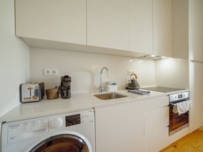 A compact kitchenette with a washing machine, a coffee maker, a kettle, and a toaster. - Apartment  by Interhome (Porto)