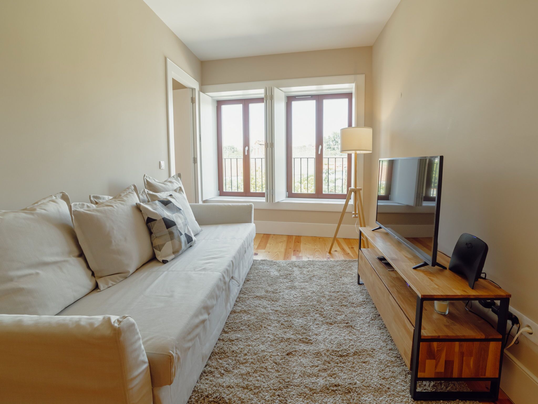 A modern bedroom with a sofa, a TV on a wooden stand, and a large window with a view.