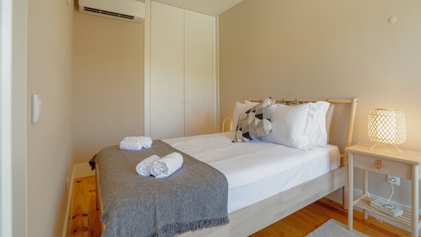 Une chambre à coucher avec un lit, une table de chevet avec une lampe, un plaid gris et des serviettes enroulées.