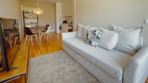 Un salon moderne avec un canapé, une table à manger et des chaises. On aperçoit un coin cuisine au fond.