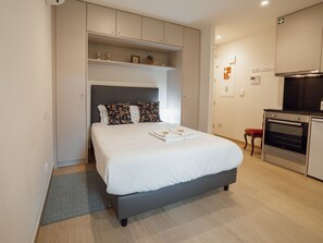 Ein modernes Schlafzimmer mit Bett, einer Einbauschränken, einer Küchenzeile und einer kleinen Sitzecke.