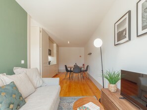 Ein modernes Wohnzimmer mit einer Couch, einem Esstisch mit Stühlen, einem Fernseher und einer Stehlampe.