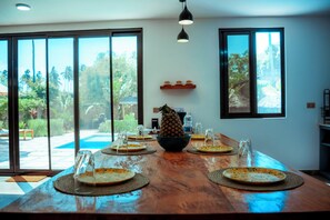 Un tavolo da pranzo con piatti, un centrotavola con ananas e vista su piscina e vegetazione.