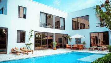 A modern two-story building with a swimming pool, sun loungers, and outdoor furniture.