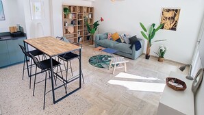 Ein modernes Wohnzimmer mit einem Holzes Esstisch, schwarzen Stühlen, einem blauen Sofa und einem großen Bücherregal.