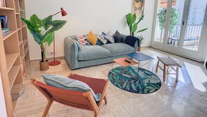 Ein stilvolles Wohnzimmer mit einer Couch, einem Couchtisch, einem Sessel, einem Bücherregal und großen Fenstern.