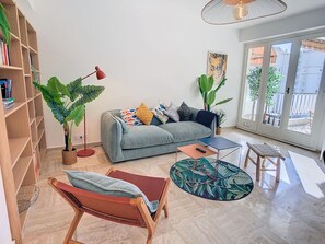 Ein stilvolles Wohnzimmer mit einer Couch, einem Couchtisch, einem Sessel, einem Bücherregal und großen Fenstern.
