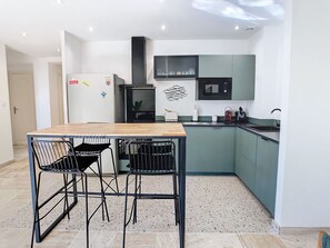 Eine kleine Küche mit Holztisch und zwei Stühlen, einer Mikrowelle und einem Kühlschrank.