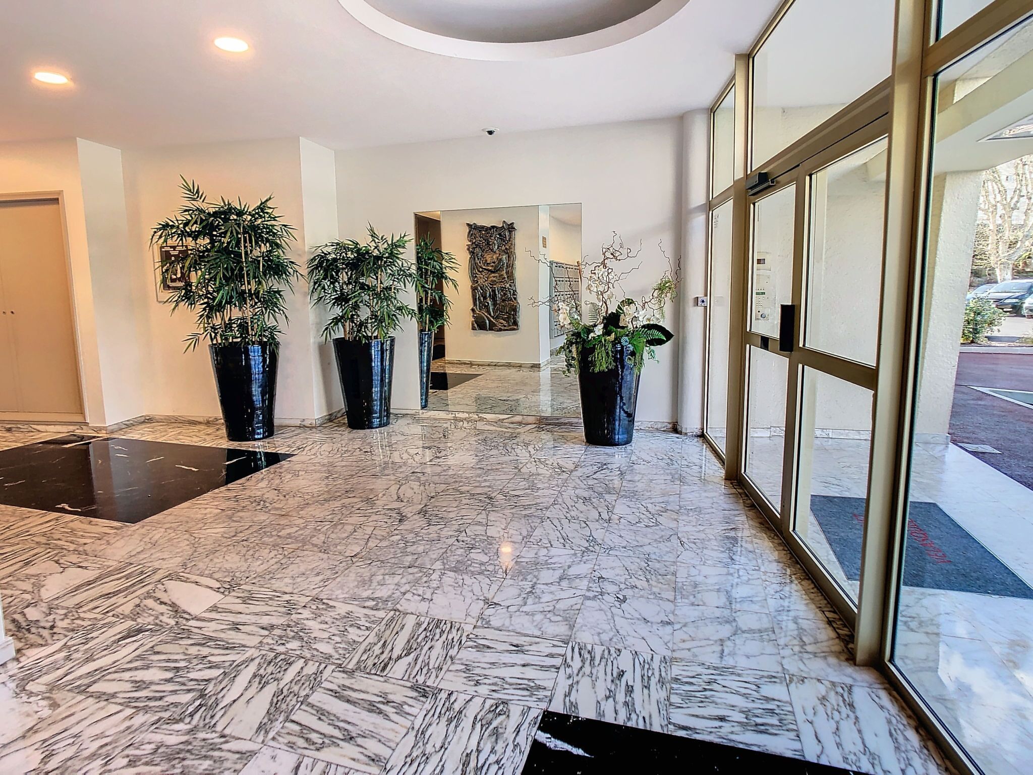 A lobby with a marble floor, potted plants, and a large glass door.