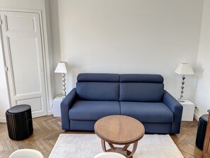 A living room with a dark blue sofa, two white side tables with lamps, a round wooden coffee table, and a white rug. - Apartment  by Interhome (Cannes)