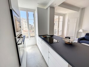 A modern kitchen with a black countertop, white cabinets, and a view of buildings through large windows. - 1 bedroom Palais Hoche Cannes Riviera 226 by Interhome (Cannes)