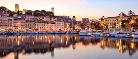 A marina with boats docked, a historic building with a clock tower, and a calm waterfront reflecting the buildings.