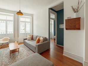 A living room with a sofa, a chair, a small table, and a hanging light fixture. - Apartment  by Interhome (Porto)