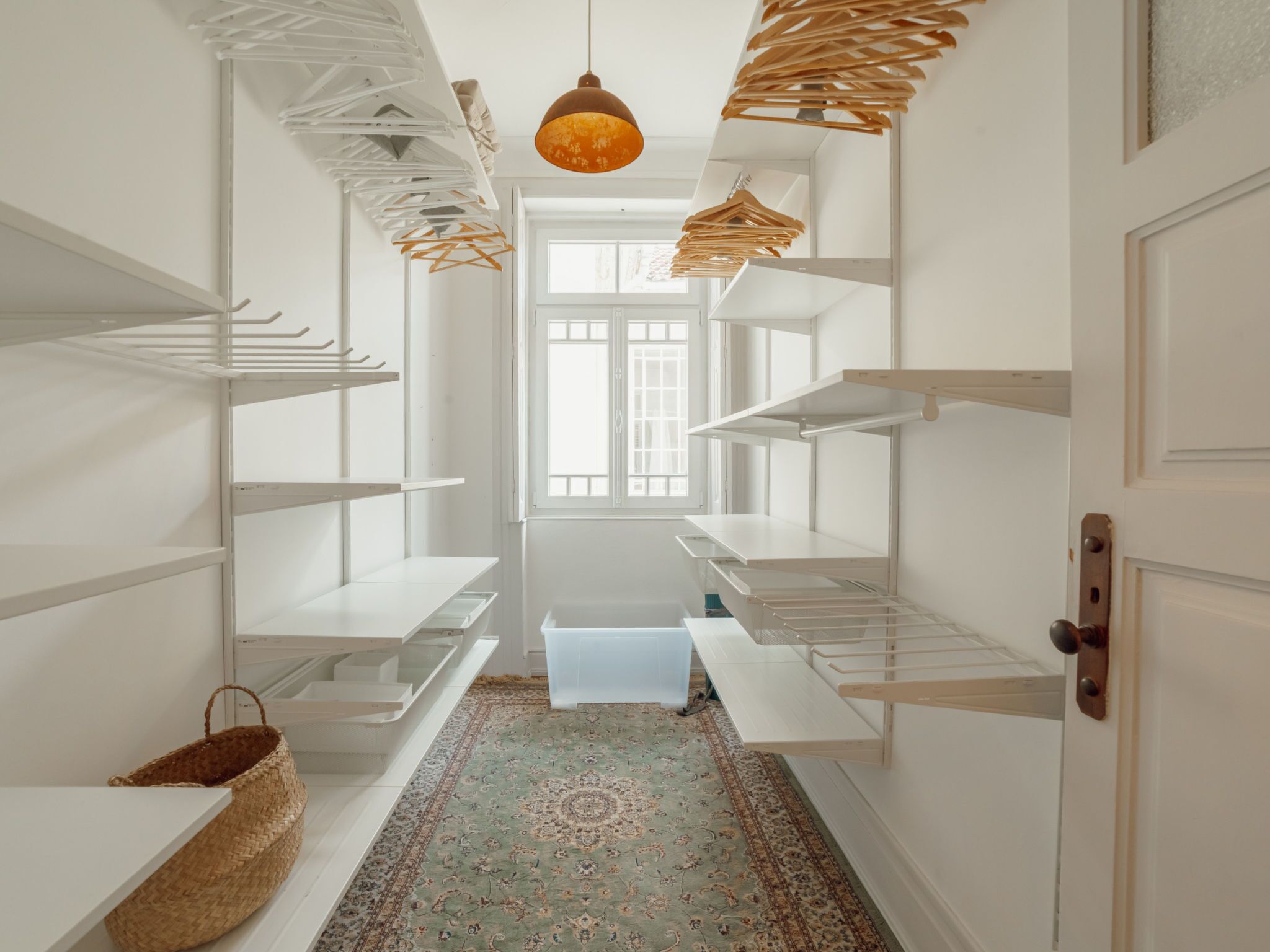 A narrow hallway with white shelving units on both sides, a patterned rug on the floor, and a hanging light fixture.