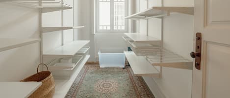 A narrow hallway with white shelving units on both sides, a patterned rug on the floor, and a hanging light fixture.