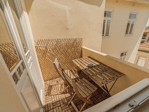 A balcony with a wooden table and chairs, a woven fence, and a view of neighboring buildings. - Apartment  by Interhome (Porto)