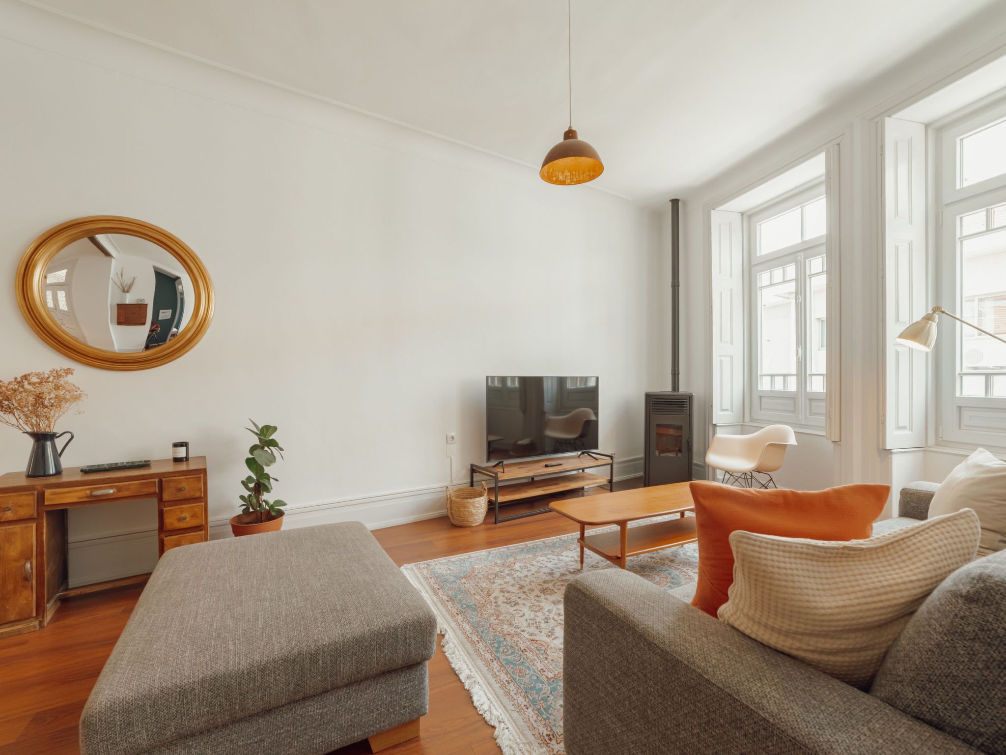 A modern living room with a sofa, ottoman, TV, and a large mirror.
