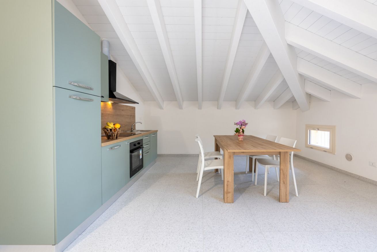 A modern kitchen with a dining area, white ceiling beams, and a small window.