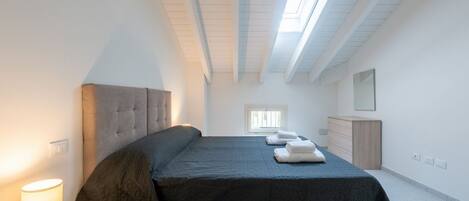 A bedroom with a bed, bedside lamp, window, and a dresser.